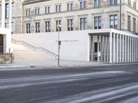 the large, empty sidewalk with multiple columns in front of the building with two signs