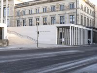 the large, empty sidewalk with multiple columns in front of the building with two signs