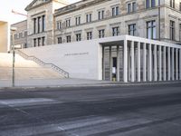 the large, empty sidewalk with multiple columns in front of the building with two signs