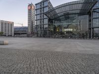 some people are walking on a brick area near a modern building with glass windows and a green street light