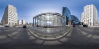 the empty intersection has a huge glass building, and some cars are moving on the road