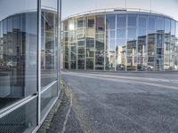 an empty road with glass buildings in the background and another building behind it that has a large mirror window on the side