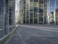 an empty road with glass buildings in the background and another building behind it that has a large mirror window on the side