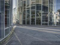 an empty road with glass buildings in the background and another building behind it that has a large mirror window on the side