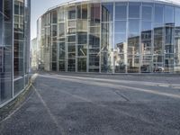 an empty road with glass buildings in the background and another building behind it that has a large mirror window on the side