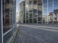 an empty road with glass buildings in the background and another building behind it that has a large mirror window on the side