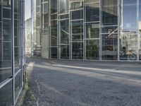 an empty road with glass buildings in the background and another building behind it that has a large mirror window on the side