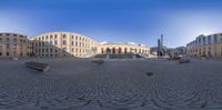 several benches in an old square outside of a large building in a city area,