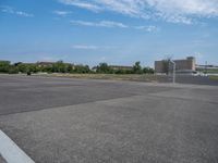 an empty parking lot with trees near by and the sky above it the pavement is smooth with white clouds in the distance