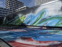 a group of people walk by some colorful art on a wall near tall buildings with metal poles