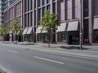 a paved city street and a brick building on the other side of it has awnings