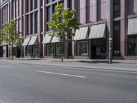 a paved city street and a brick building on the other side of it has awnings