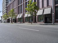 a paved city street and a brick building on the other side of it has awnings