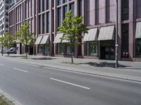 a paved city street and a brick building on the other side of it has awnings