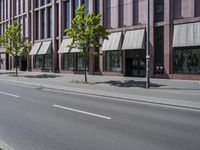 a paved city street and a brick building on the other side of it has awnings