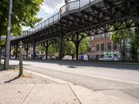 this is a city street under a bridge on a sunny day with parked cars, and people walking along