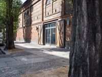 a sidewalk next to a building with a large tree in the foreground and some windows