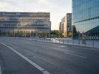 an empty city street lined with tall buildings and a fenced in parking lot to the side