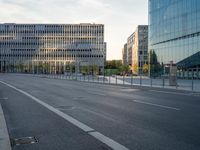 an empty city street lined with tall buildings and a fenced in parking lot to the side