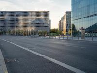 an empty city street lined with tall buildings and a fenced in parking lot to the side