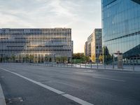 an empty city street lined with tall buildings and a fenced in parking lot to the side