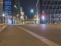 an empty city street with some traffic lights at night time in front of large buildings