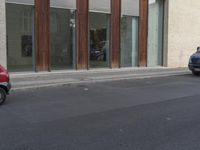 a person riding a skateboard on the sidewalk near a building with windows and a sign reading no standing here