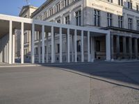 the large, empty sidewalk with multiple columns in front of the building with two signs