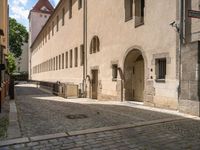 a cobblestone sidewalk is shown with benches and buildings in the background, where people walk along the sidewalk