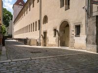 a cobblestone sidewalk is shown with benches and buildings in the background, where people walk along the sidewalk