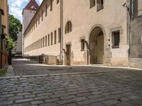 a cobblestone sidewalk is shown with benches and buildings in the background, where people walk along the sidewalk