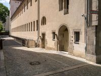 a cobblestone sidewalk is shown with benches and buildings in the background, where people walk along the sidewalk