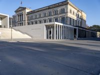 the large, empty sidewalk with multiple columns in front of the building with two signs