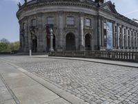 large building with intricately designed roof and windows in a city area with cobblestone street in front