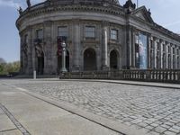 large building with intricately designed roof and windows in a city area with cobblestone street in front