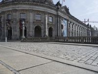 large building with intricately designed roof and windows in a city area with cobblestone street in front