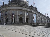 large building with intricately designed roof and windows in a city area with cobblestone street in front