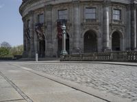 large building with intricately designed roof and windows in a city area with cobblestone street in front