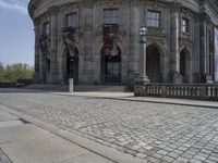 large building with intricately designed roof and windows in a city area with cobblestone street in front