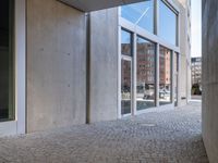 an empty cobblestone walkway outside a large building with large windows on one side