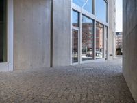 an empty cobblestone walkway outside a large building with large windows on one side