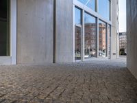 an empty cobblestone walkway outside a large building with large windows on one side