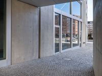 an empty cobblestone walkway outside a large building with large windows on one side