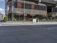 a grey building sitting next to a street corner next to trees and bushes on the side of the road