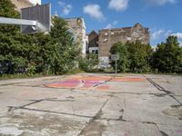 a dirty parking lot with a basketball court and graffiti on the ground and buildings in the background