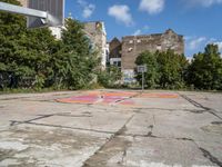 a dirty parking lot with a basketball court and graffiti on the ground and buildings in the background