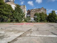 a dirty parking lot with a basketball court and graffiti on the ground and buildings in the background