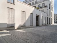 people walking through an old city sidewalk in the sun and shadows on the building windows