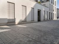 people walking through an old city sidewalk in the sun and shadows on the building windows