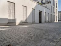 people walking through an old city sidewalk in the sun and shadows on the building windows